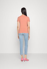 Kortärmad peach t-shirt med en figurnära silhuett, ihop med ljusblå jeans och rosa klackskor, sedd bakifrån.