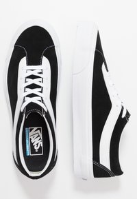 Černobílé tenisky Vans s bílými tkaničkami, bočním pruhem a bílými gumovými podrážkami, zobrazené z vrchu a bočního pohledu na bílém pozadí.