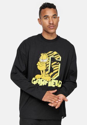 Camiseta negra de manga larga con un gran gráfico de Garfield en amarillo y verde con el texto "G" y "GARFIELD". Hecha de suave tela de algodón.