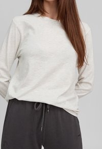 Lys grå langærmet top i et blødt materiale, med en rund halsudskæring og afslappet pasform, parret med mørke grå sweatpants med snørre.