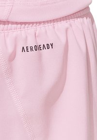 Pantaloni sportivi di un delicato rosa chiaro realizzati in tessuto morbido. Presentano un elastico in vita e il marchio "AEROREADY" in nero. Dettagli delle cuciture visibili.
