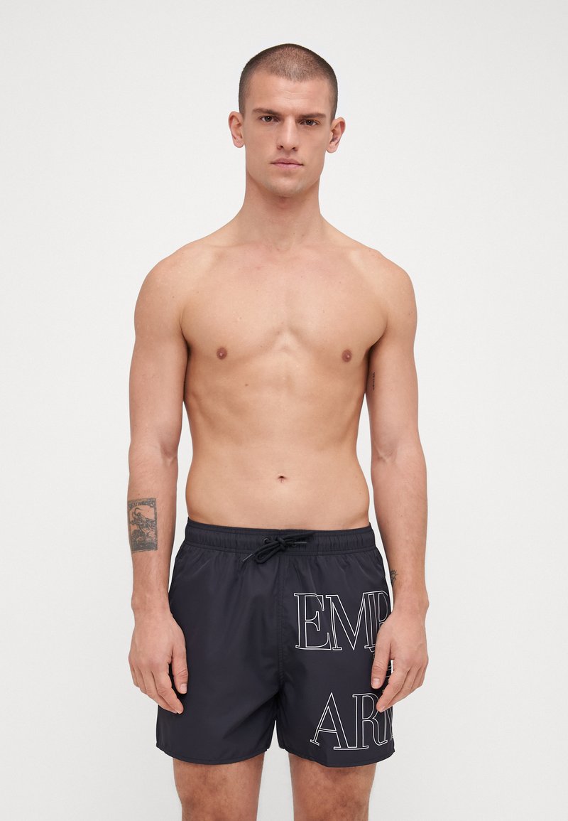 Shorts de bain noirs avec l'inscription blanche "EMB", taille élastique et cordon de serrage. Fabriqués en matériau léger, avec une texture lisse.