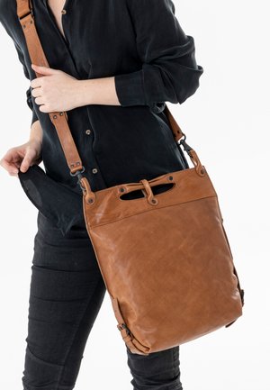 Braune Leder-Umhängetasche mit strukturierter Oberfläche, verstellbarem Tragegurt und durchbrochenen Akzenten. Das Design ist rechteckig mit einem oberen Verschluss.