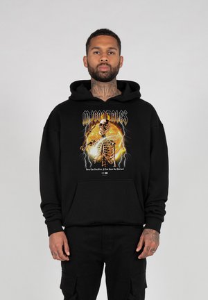 Sort hættebluse med et skeletgrafik mod en orange baggrund, med "M. Gonzales" tekst ovenfor og en indskrift nedenfor. Fremstillet i bomuldsstof, med løs pasform.