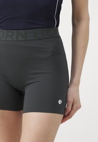 Svart trening shorts med bred elastisk midjebånd som har "BORN" tekst. Glatt tekstur og tettsittende design med en liten hvit logo-detalj.