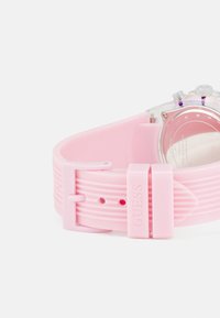 Rosa Silikonarmbanduhr mit klarem Gehäuse, rundem Zifferblatt und einer Schnalle mit geprägtem "GUESS". Strukturelle Akzente am Armband.