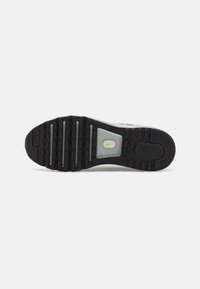 Semelle de chaussure avec une bande de roulement noire comprenant des rayures horizontales et une petite section blanche au milieu avec un logo Nike swoosh jaune.