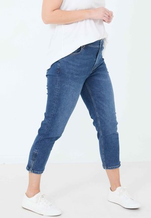 Denim jeans in een middelblauwe was met een slim fit, cropped lengte en opgerolde mouwen. Gemaakt met witte sneakers en een losse witte top.