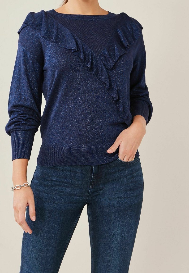 Pull bleu marine avec des volants au niveau du col, fabriqué dans un matériau texturé avec un léger éclat. Manches longues et poignets côtelés.