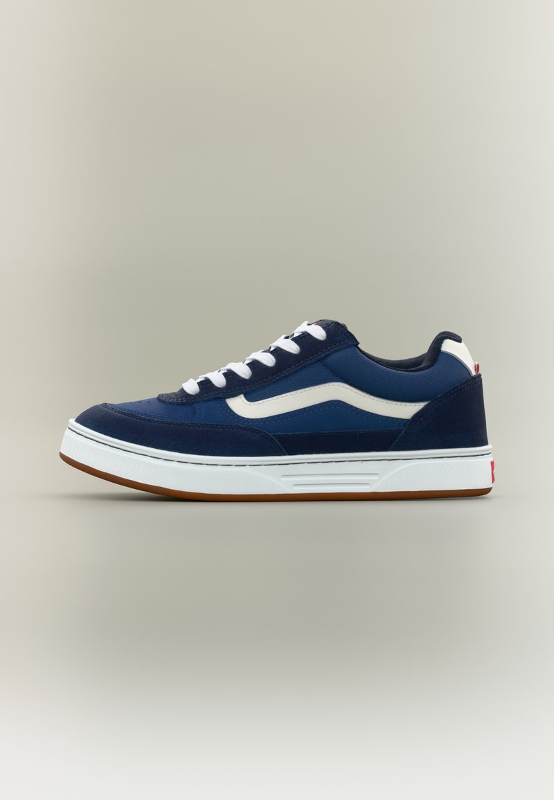 Παπούτσι τύπου χαμηλό sneaker σε σκούρο μπλε χρώμα με λευκή λωρίδα στο πλάι, λευκά κορδόνια και χοντρή λευκή σόλα με καφέ πέλμα.