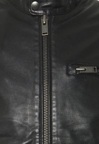 Svart läderjacka med centralt silverfärgat blixtlås och en liten horisontell ficka med blixtlås på högra sidan.