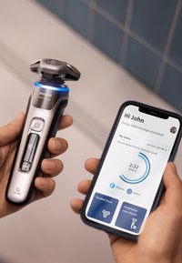 Philips 9000 Prestige elektrische scheerapparaat met een zilver en zwart ontwerp, uitgerust met een blauwe LED-indicator en gekoppeld aan een smartphone-appweergave.