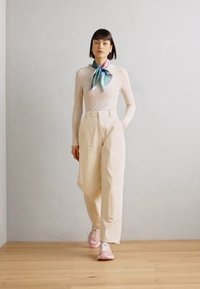 Pale pink long-sleeve top, cream wide-leg pants, and light pink sneakers. A silk scarf with green and blue hues tied at the neck.