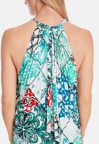 Sleeveless halter top featuring a mix of turquoise, red, and black patterns with pleated texture and a drawstring closure at the neckline.