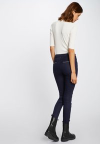 Jeans ajustados azul marino con detalles de costura, combinados con una blusa de canalé ligera. La modelo lleva botines negros con suela gruesa.