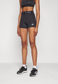 Zwarte sportshorts met een gladde textuur en een elastische tailleband, voorzien van een wit "TECHFIT" logo en drie witte strepen aan de zijkant.