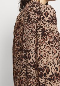 Leopard-Print-Bluse in Beige und Braun, aus weichem Stoff, mit lässiger Passform und Falten-Details an der Schulter.
