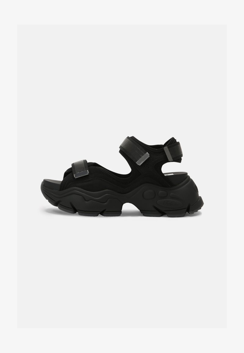 Black sandals with a chunky rubber sole, featuring soft straps and adjustable Velcro closures. Made of synthetic materials with a textured finish.