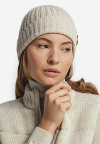 Strikket lys beige hue med lodret ribstruktur; båret med en højt krave, cremet sweater. Har et lille accentdetalje på siden.