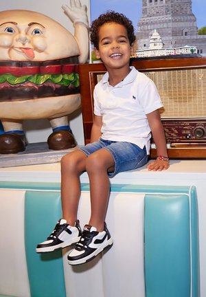 Zwart-witte sneakers met een rode accenten, denim shorts en een wit polo-shirt. Zittend naast een cartoon hamburger figuur.