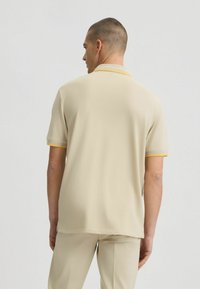 Beige Poloshirt mit gelbem Besatz am Kragen und an den Ärmeln, aus einem glatten Stoff gefertigt. Die Rückseite hat ein einfaches, cleanes Design.