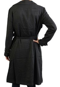 Manteau noir en trench-coat avec une taille ceinturée, des manches longues et un col à revers. Fabriqué en tissu lisse, montrant de légères rides et plis.