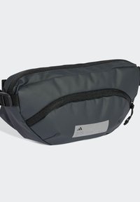 Borsa a vita grigia realizzata in materiale resistente, dotata di una tasca frontale con zip, cinturino regolabile e un logo discreto su una toppa testurizzata.