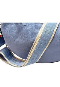 Ronde, lichtblauwe leren tas met een textuur; beschikt over een decoratieve strap in blauw en beige met een geometrisch patroon.