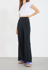 Vita byxor med vida ben och ribbad struktur i svart tyg, med elastisk midjeband. Matchas med ljuslila skor med gummisula och vita ränder.