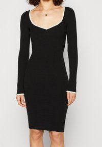 Robe noire à manches longues avec un décolleté en V profond et des finitions crème contrastantes au niveau de l'encolure et des poignets ; silhouette cintrée.