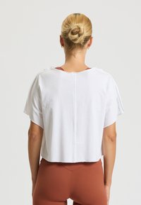 Izrezana bela majica iz mehke tkanine, z kratkimi rokavi, zadnjim šivom in rahlim nabiranjem na ramenih.