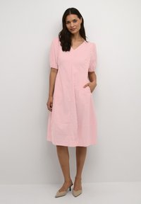 Pink striped dress with short, puffed sleeves, V-neckline, and pockets. Smooth texture with a flowing shape, featuring a gathered skirt.