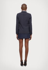 Taillierter navyblauer Blazer mit strukturiertem Finish, figurbetontem Schnitt und Ein-Knopf-Verschluss; kombiniert mit einem Minirock und schwarzen Absatzschuhen.