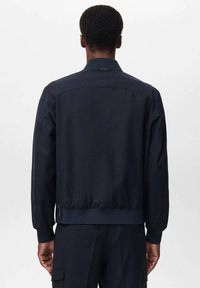 Tummansininen pommikauppalaisjacket, jossa on uritettu kaulus ja hihansuut, omaa sileän pinnan ja joustavan vyötärön. Yksinkertainen muotoilu ilman kuvioita tai koristeita.