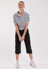 Zwarte cropped broek gecombineerd met een wit en marineblauw gestreepte polo, met een kraag. Sneakers maken de outfit compleet.