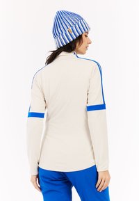 Crème lange mouwen top met blauwe accenten en strepen, gemaakt van een gladde stof; gecombineerd met een blauw-wit gestreepte gebreide beanie.