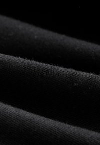 Juoda medžiaga su minkštu, tekstūruotu paviršiumi. Matomi siūlai ir pluoštai, pabrėžti arti fiksuojant subtilų blizgesį.