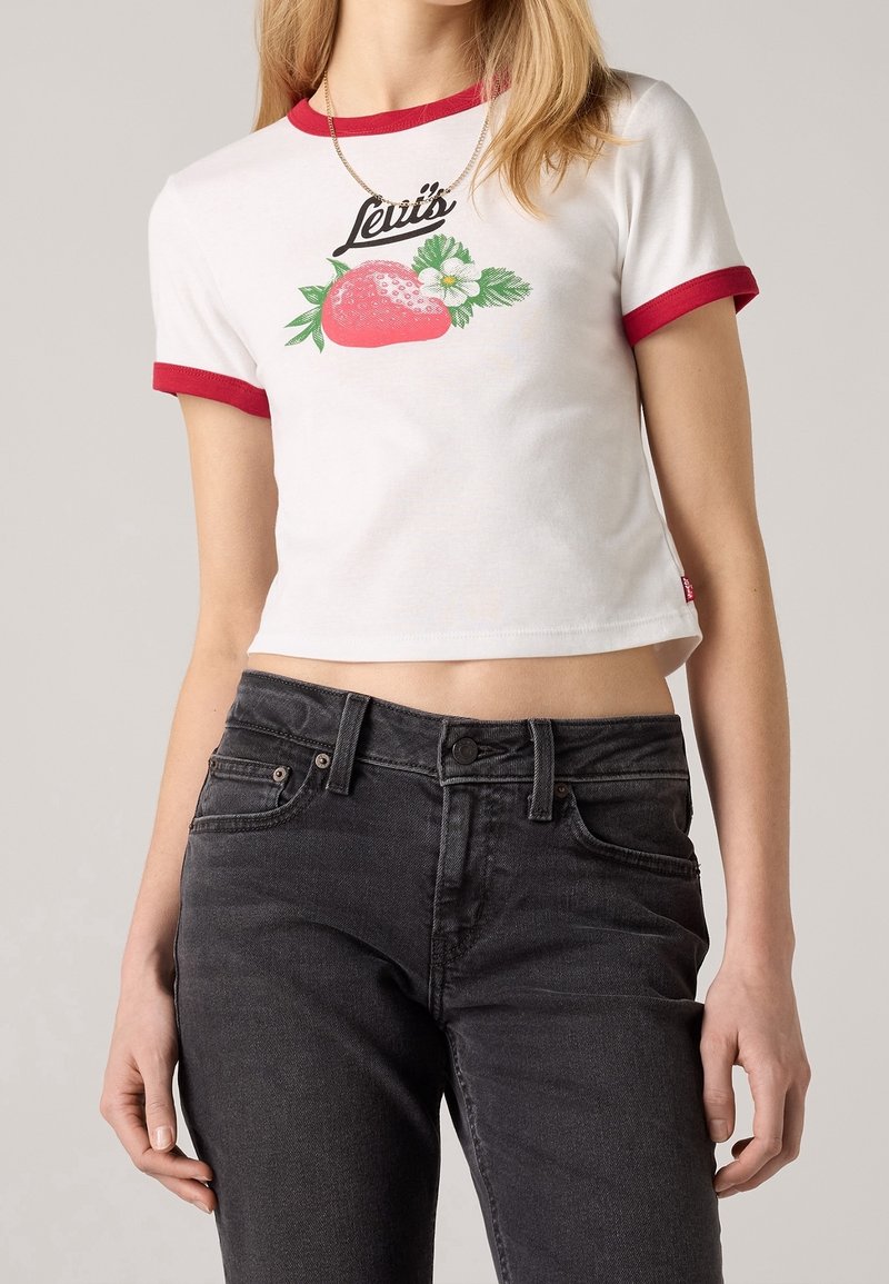 Camiseta blanca recortada con cuello rojo y gráfico grande de una fresa, con el texto "Levi's" arriba. Combinada con jeans oscuros.