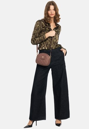 Groene blouse met panterprint en een satijnen uitstraling; loszittende brede broekspijpen van donker denim; kleine, gewatteerde bruine crossbodytas; zwarte pumps met een spits toe.