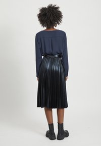 Blusa blu navy con scollatura a barco, abbinata a una gonna nera plissè e stivaletti neri, caratterizzati da una texture liscia e lucida.