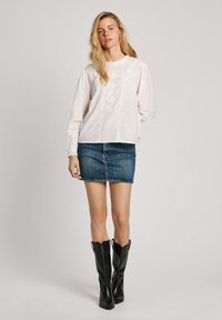 Blusa bianca a maniche lunghe con dettagli testurizzati, abbinata a una minigonna di denim e stivali neri in pelle alti fino al ginocchio. Design e vestibilità semplici.