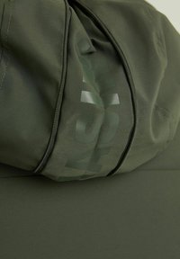 Borsa verde con cerniera in tessuto strutturato; presenta un grande logo lucido in una tonalità di verde più scura su un lato.