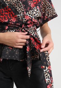 Sort indpakningstop med røde blomster- og leopardprintmønstre, med en bælte i taljen og korte ærmer. Fremstillet af glat stof.