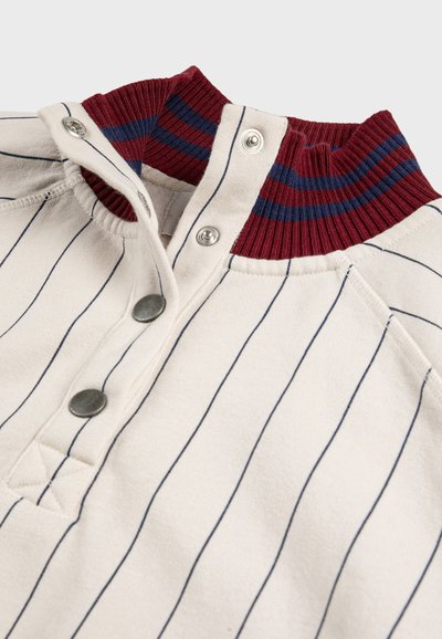 Chemise couleur crème avec de fines rayures verticales bleu marine, boutons-pression en métal, et un col côtelé bordeaux avec des rayures bleu marine.