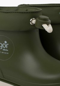Botas de lluvia de goma verdes con una superficie texturizada, logo redondo y forro. Cuentan con un ajuste ceñido en la parte superior enrollable con detalles decorativos de cuerda blanca y botón.
