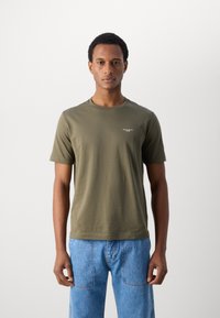 Oliven grønt kortærmet t-shirt lavet af blødt bomuld med rund hals. Har et lille logo på venstre bryst. Kombineret med blå jeans.