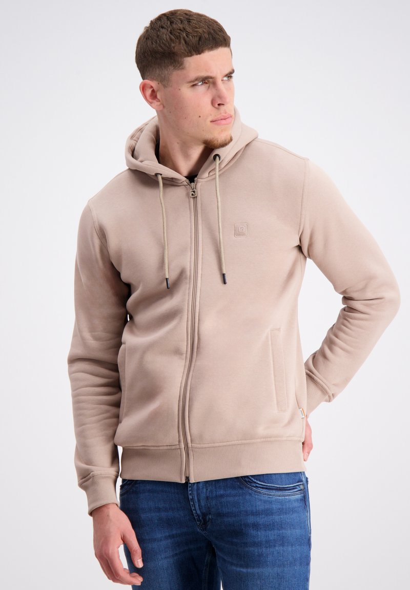 Šviesiai ruda zip-up džemperis su kapisonu, reguliuojamu raišteliu, gumuotais rankogaliais ir kišenėmis, pagamintas iš minkštos medžiagos, su subtiliai iššūsnorintu logotipu ant krūtinės.