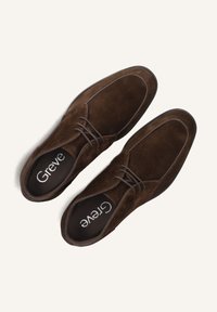 Chaussures en daim marron avec des bouts arrondis et des lacets. Présentent des coutures blanches le long des bords. La marque à l'intérieur indique "Greve". Texture lisse.