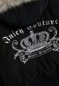 Черно яке отзад със сребърна бродирана корона и текст "Juicy Couture" и "Girlie Royalty" под качулка с кожена облицовка.