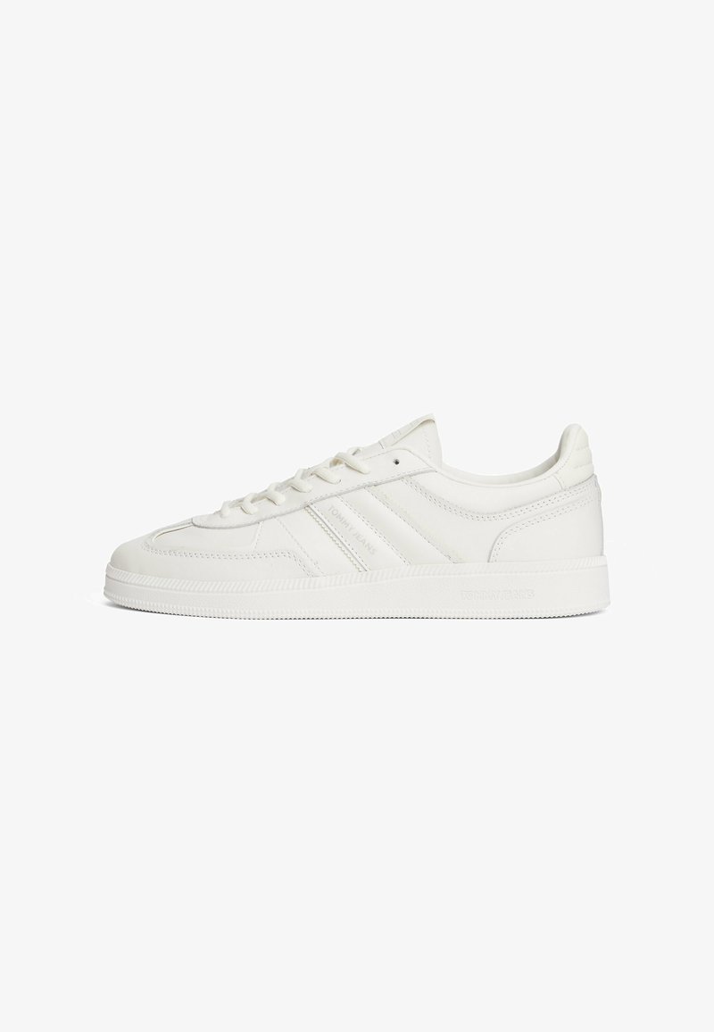 White leather sneaker with textured upper, logo accents, rounded toe, flat laces, and a rubber sole featuring horizontal grooves.